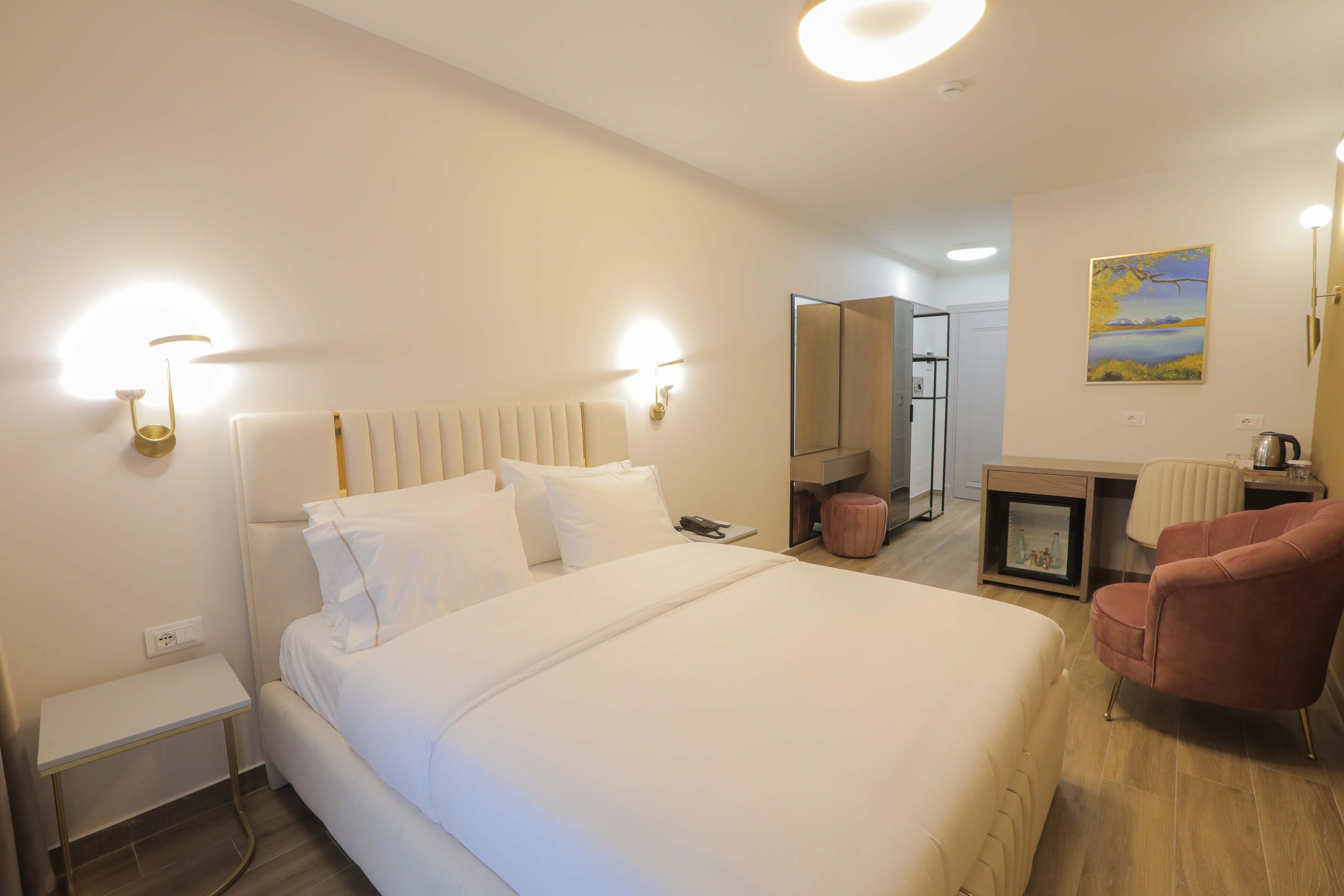 A hotel room with a large bed, bedside tables, a chair, a desk, and a mirror.