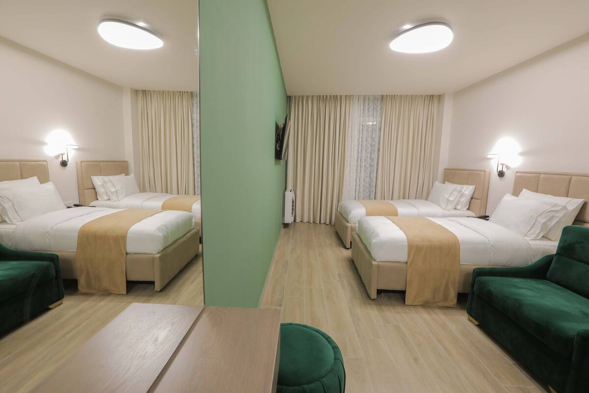 A hotel room with two beds, a green sofa, a wooden table, and a mirror.