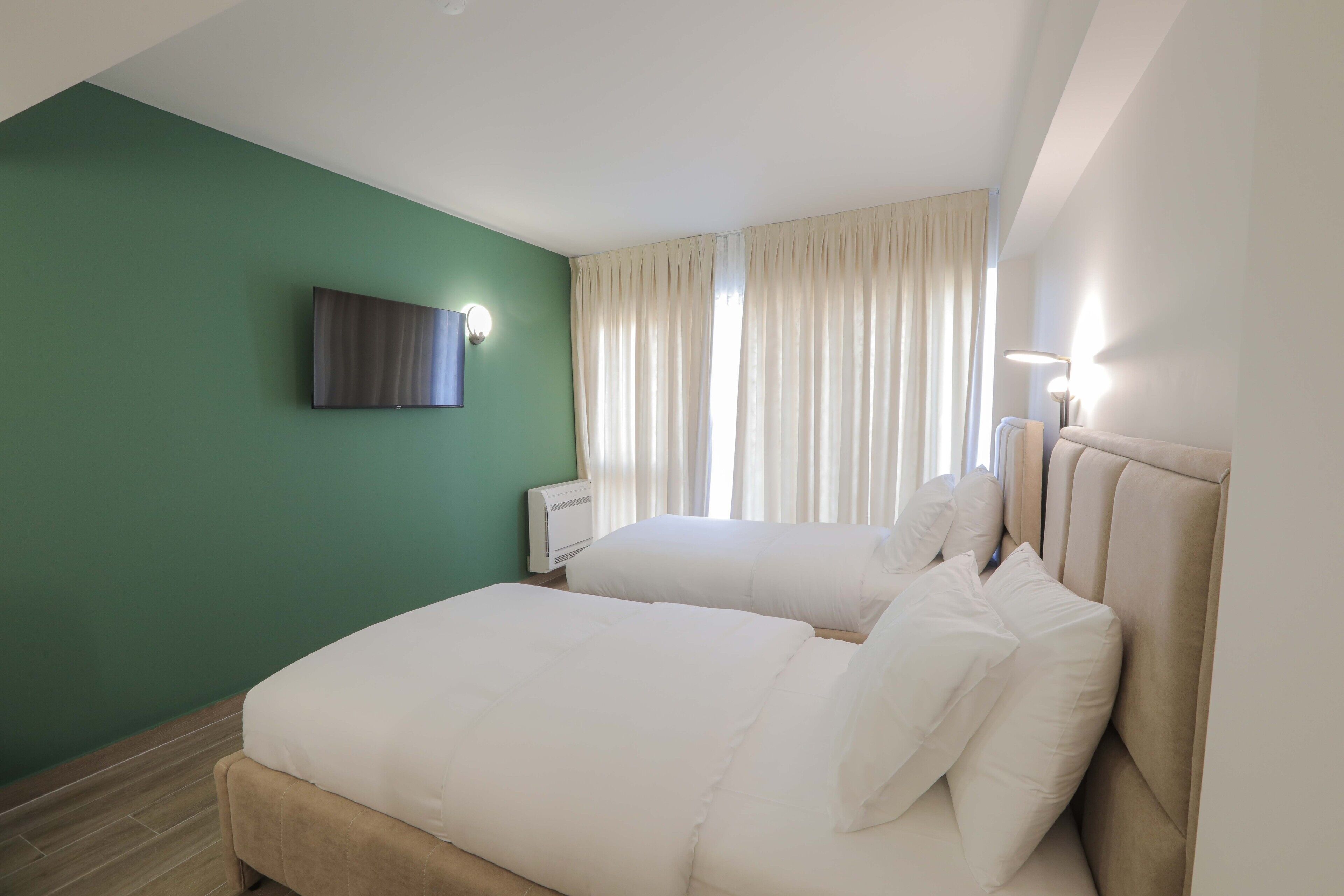 Une chambre d’hôtel avec deux lits, un téléviseur à écran plat fixé au mur et une fenêtre avec des rideaux.
