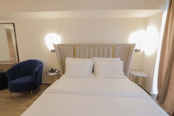 A hotel room with a large bed, a blue armchair, bedside tables with lamps, and a mirror on the wall.