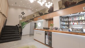 A modern hotel reception area with a staircase, a reception desk, and a bar with various liquor bottles. - Olia Residence (Tirana)
