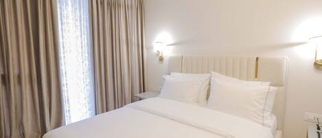Quarto de hotel com uma cama grande, mesa de cabeceira, abajur e janela com cortinas.