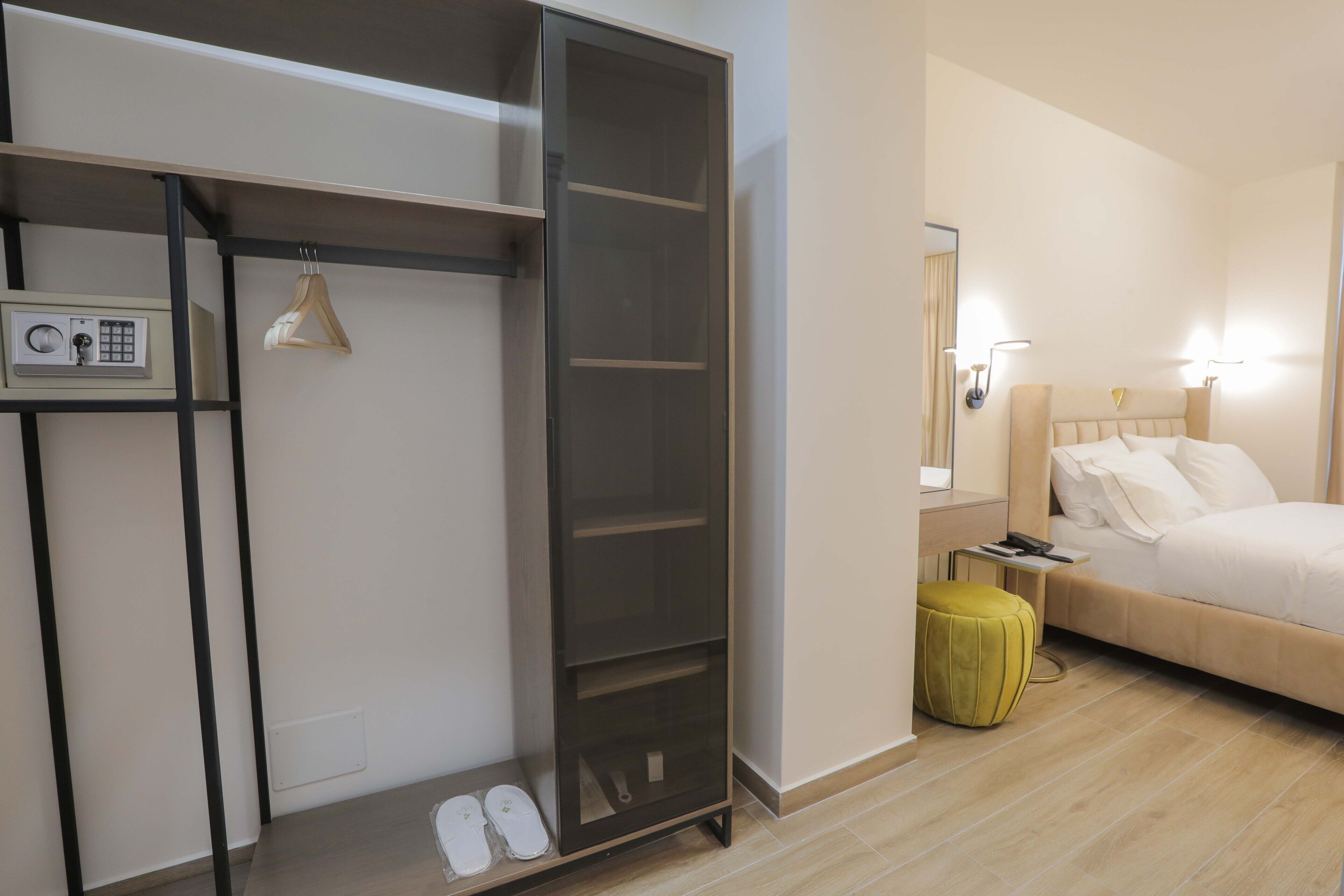 Ein Hotelzimmer mit Bett, Schrank, Nachttisch mit Lampe und einem kleinen Hocker.