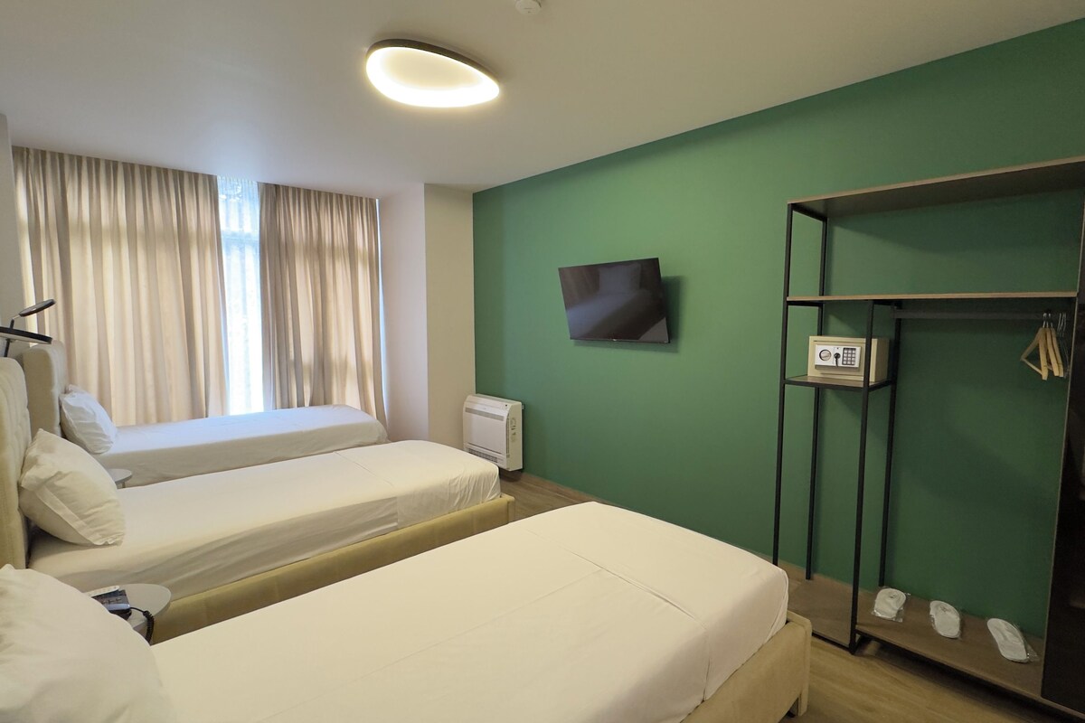 A hotel room with two beds, a TV, a wardrobe, and a window with curtains.