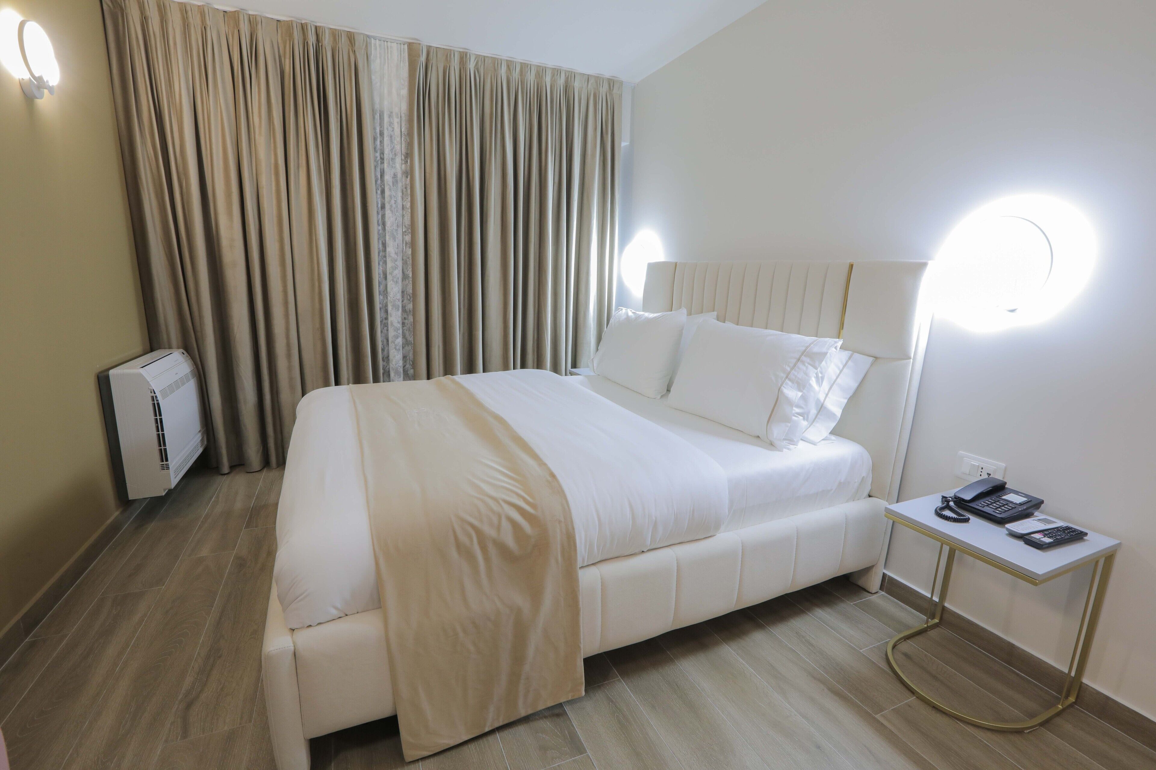 A neatly arranged hotel room with a large bed, a bedside table with a lamp, and a wall-mounted light fixture.