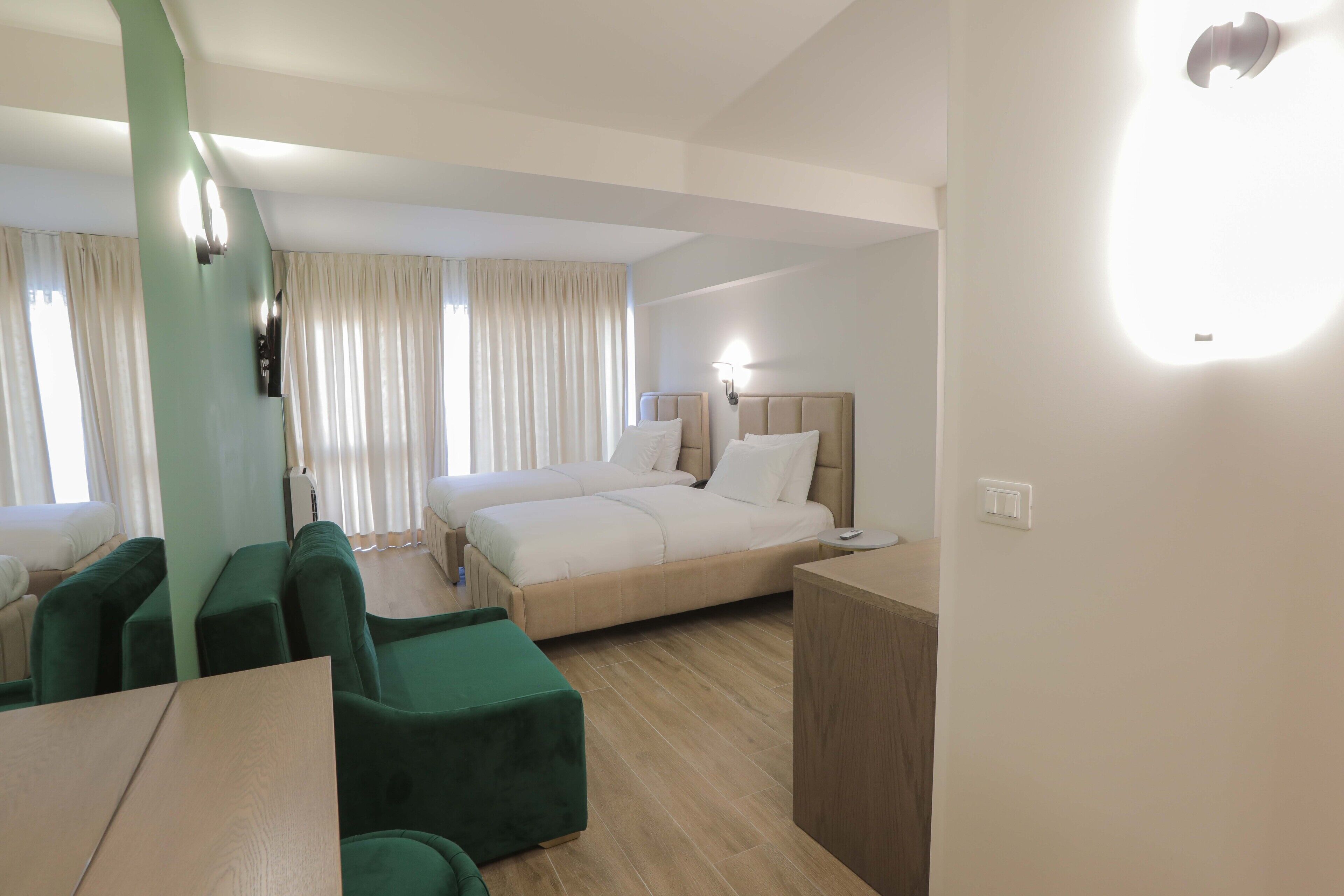 A hotel room with a bed, a desk, and two green armchairs.