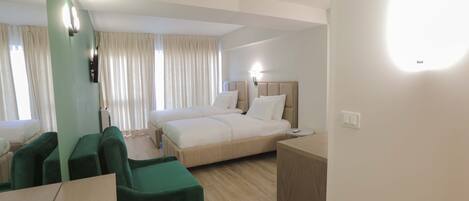 A hotel room with a bed, a desk, and two green armchairs.