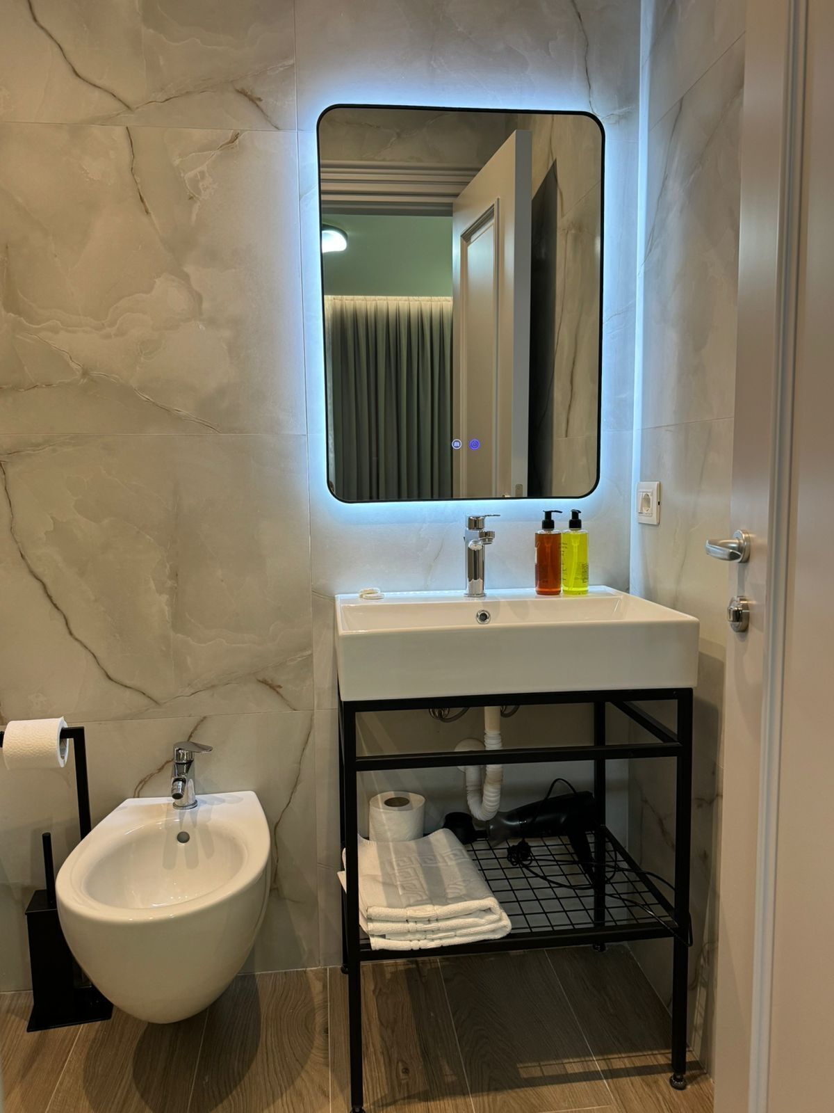 Un baño con pared de mármol, un lavabo blanco con espejo, un bidé y un perchero para toallas.