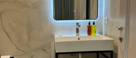 Un baño con pared de mármol, un lavabo blanco con espejo, un bidé y un perchero para toallas.