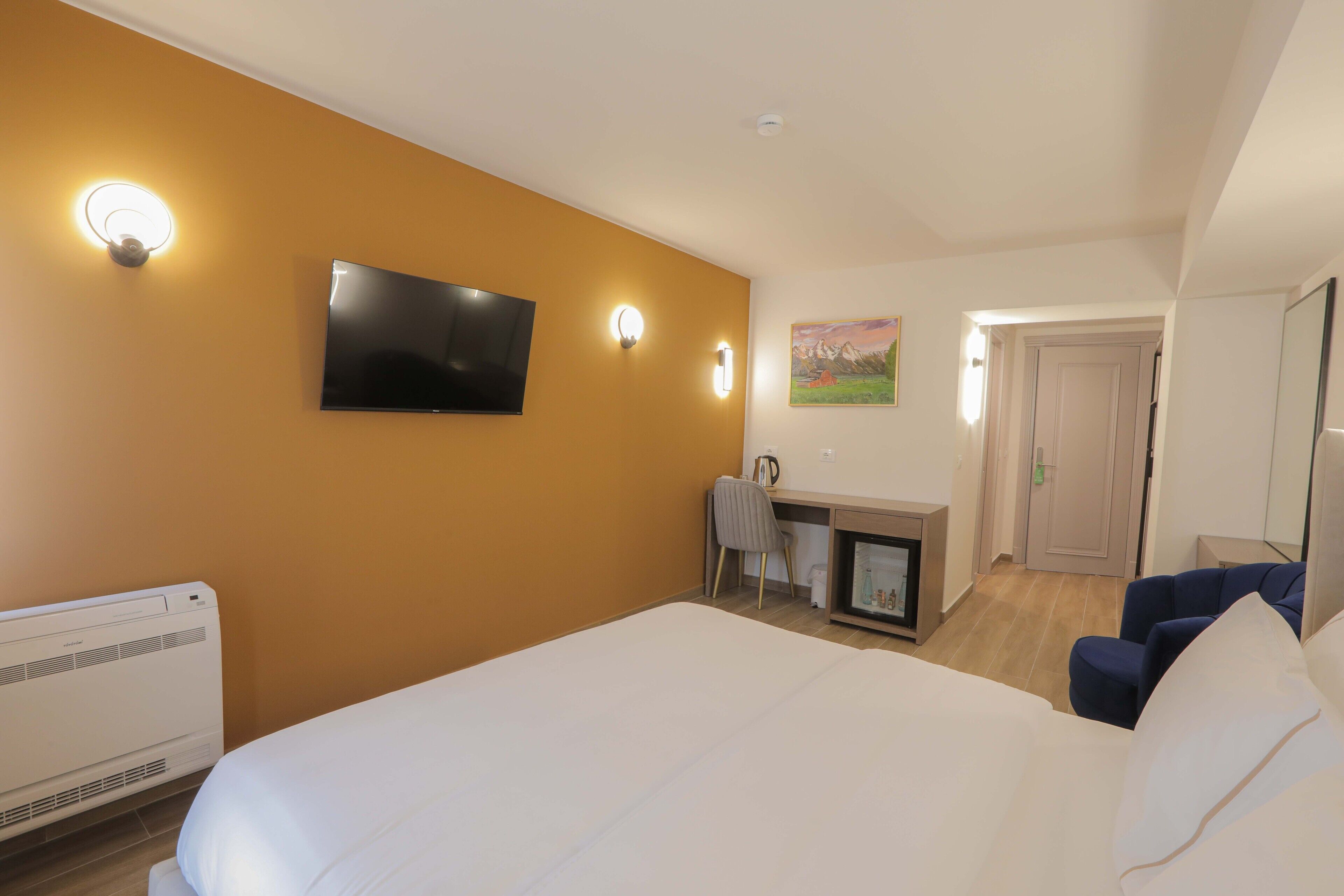 A hotel room with a bed, a desk, a chair, a TV, and a painting on the wall.