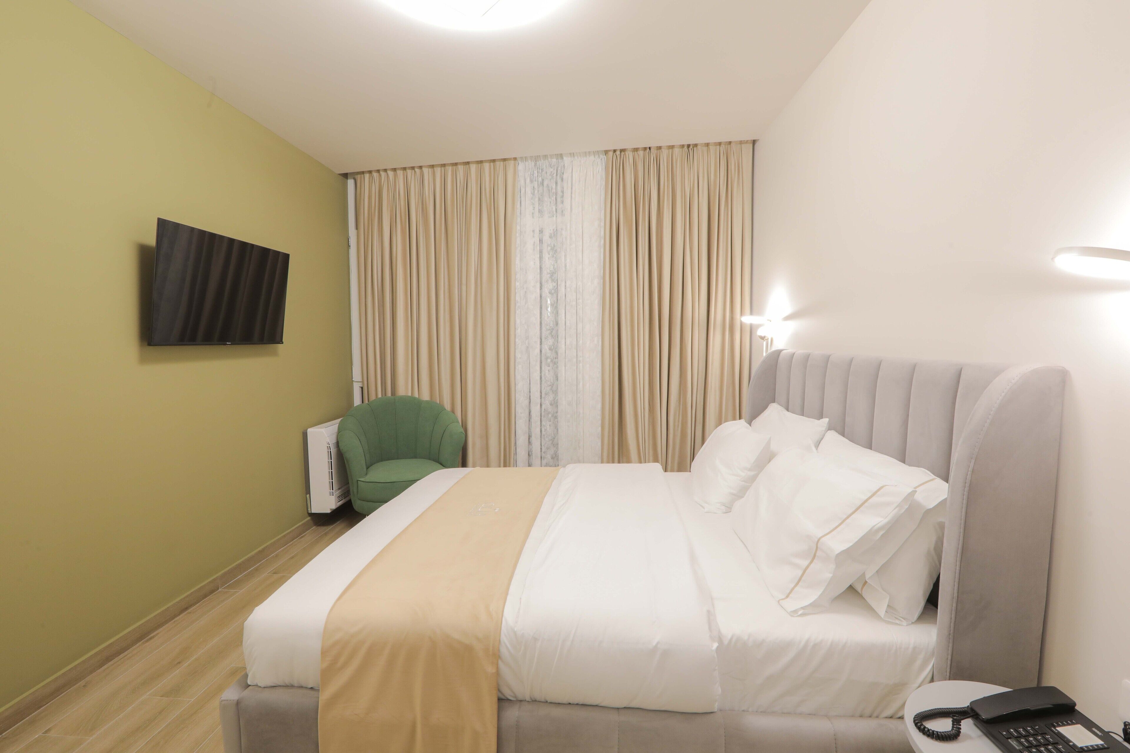Ett hotellrum med en säng, en grön stol, en platt-TV och en telefon.