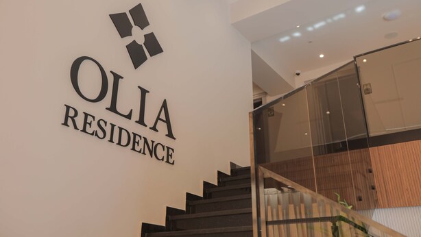 A staircase with a glass railing and a wall with the text "OLIA RESIDENCE". - Olia Residence (Tirana)