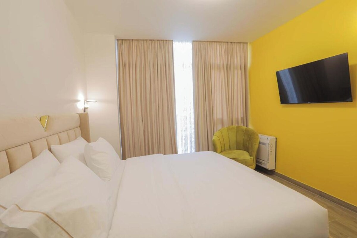 A hotel room with a large bed, a flat-screen TV mounted on the wall, and a chair.