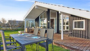 Ein modernes Haus mit überdachter Terrasse, Sitzgelegenheit im Freien und einem großen Fenster mit Blick auf den Garten.