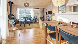 Ein gemütliches Wohnzimmer mit Kamin, ein Essbereich mit Holztisch und Stühlen sowie eine Küchenzeile mit einer großen, weißen Pendelleuchte.