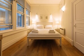 A neatly arranged bedroom with a large bed, bedside lamps, and a window with blinds.