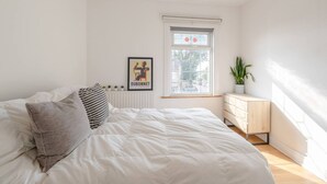 Et soveværelse med en stor seng, et vindue, en radiator, en kommode og et billede i ramme på væggen.
