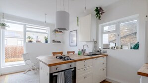 Et moderne køkken med hvide skabe, en træbordplade og en indbygget ovn. To stole, en vask og et vindue med udsigt til en murstensmur.