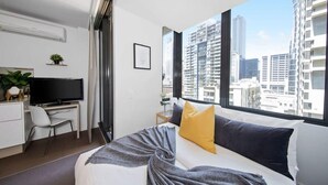 A modern hotel room with a bed, a desk, a TV, and a large window with a city view. - Cozy & Modern Studio Right Next to Southern Cross (Melbourne)