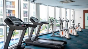 Une salle de sport équipée de tapis de course et de vélos d’appartement, dotée de grandes fenêtres et d’un sol recouvert d’une moquette bleue.