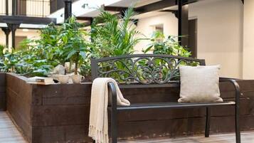 A wooden bench with a cushion, surrounded by greenery and a wooden planter.