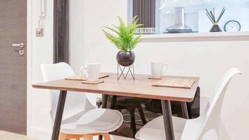A dining area with a wooden table, white chairs, and a potted plant.