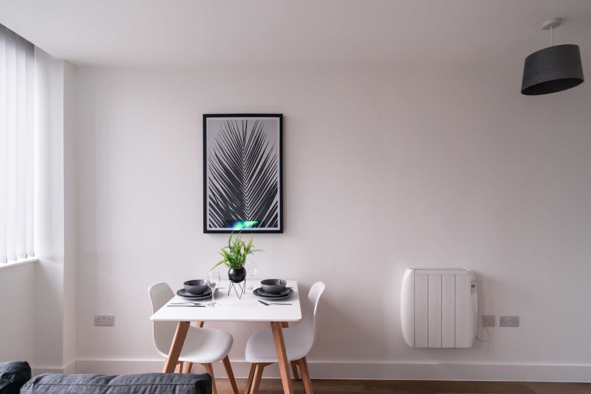 Un comedor moderno con una mesa blanca, platos negros y una planta en maceta.