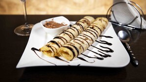 A plate of crepes with chocolate sauce, a small bowl of sauce, and a wine glass. - Golden Beach Cottages (Trincomalee)