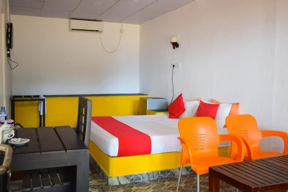 A hotel room with a bed, a desk, and two orange chairs.