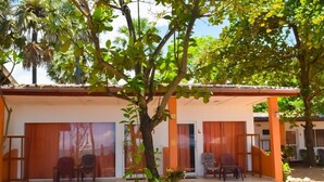 A building with a covered porch, two chairs, and a tree in front. - Golden Beach Cottages (Trincomalee)