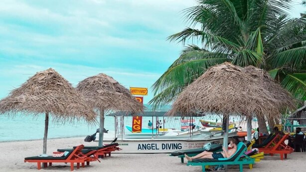 A beach with thatched umbrellas, lounge chairs, and a sign for 'Angel Diving'. - Golden Beach Cottages (Trincomalee)
