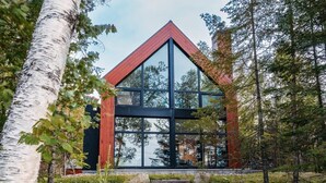 A modern cabin with a triangular roof, large windows, and a natural forest setting.