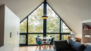 A modern loft bedroom with a large skylight, a cozy seating area with a sofa and chairs, and a bookshelf.