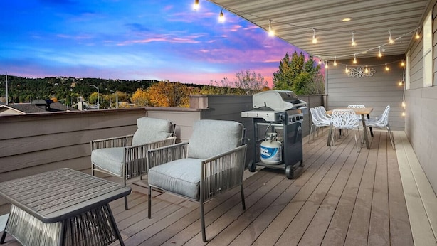 Une terrasse sur le toit, aménagée avec du mobilier d’extérieur, un barbecue et des guirlandes lumineuses, le tout sur fond de coucher de soleil.