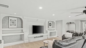 Un salon moderne doté d’un téléviseur à écran plat, d’étagères intégrées, d’un canapé en cuir et d’un ventilateur de plafond.