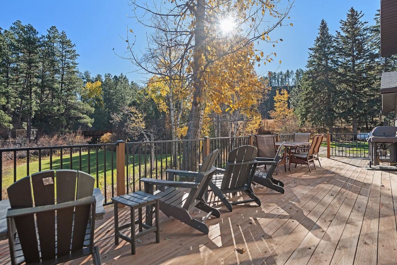 Een houten terras met Adirondack-stoelen, een barbecue en uitzicht op een golfbaan.