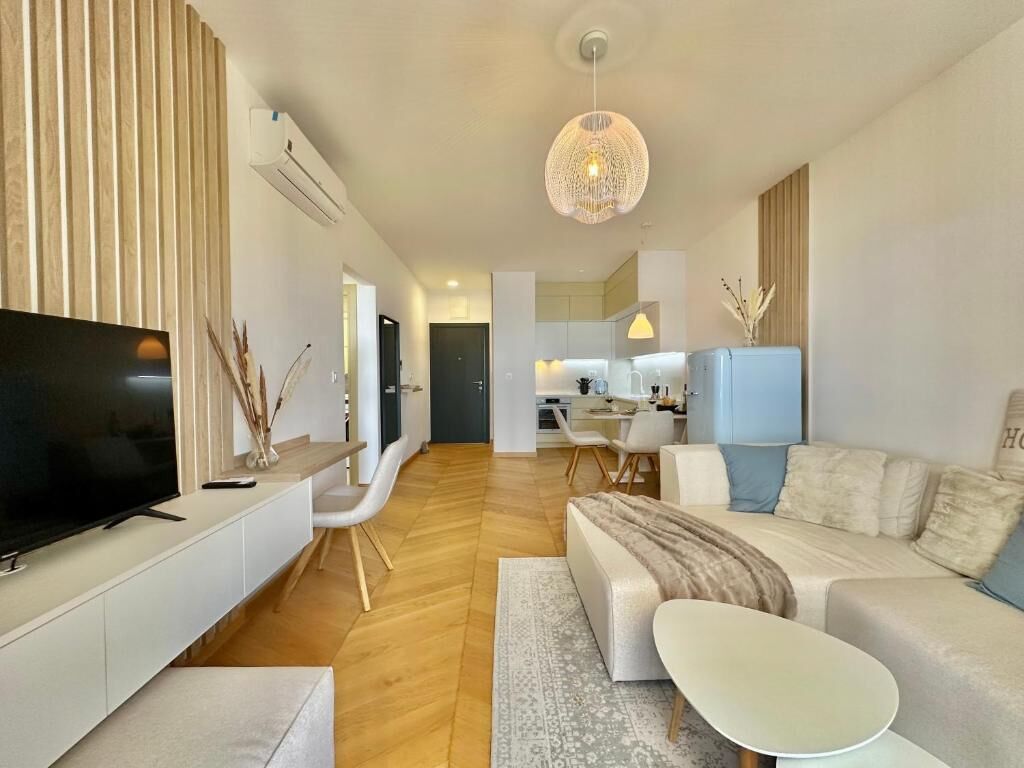 A modern living room with a flat-screen TV, a sofa, a coffee table, and a dining area in the background.