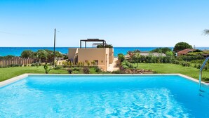 A swimming pool with a clear view of the ocean and a modern building in the background. - Villa with pool, on the sea in Marina di Modica (Marina di Modica)