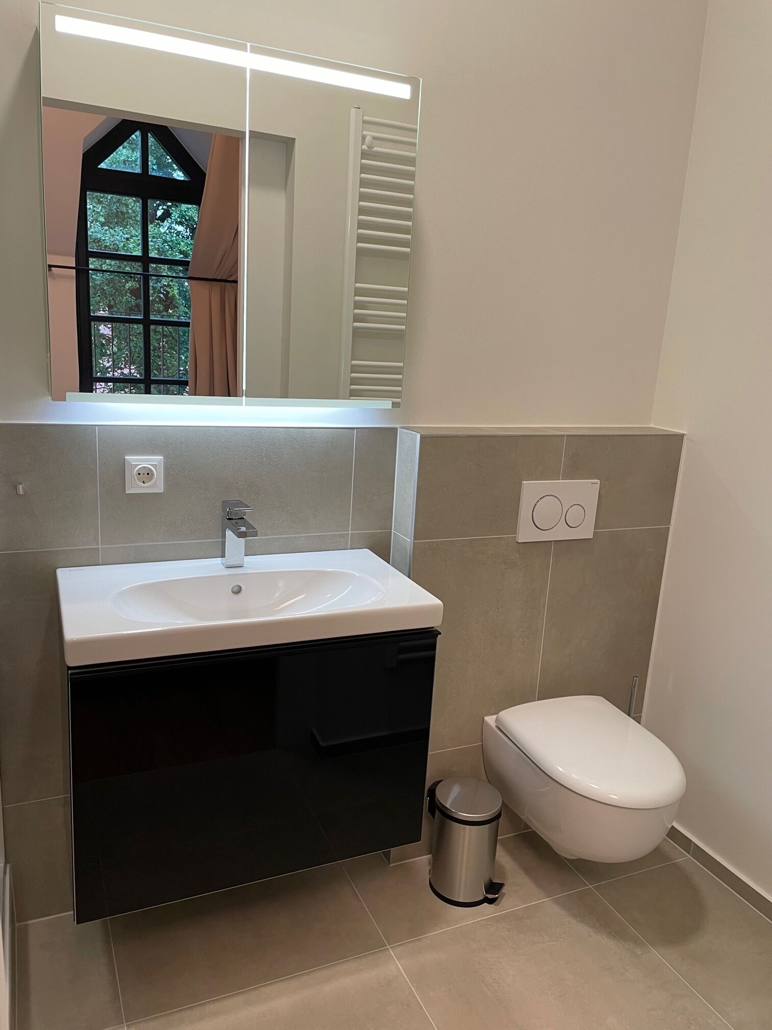 Un baño con un lavamanos blanco, un espejo, un inodoro y un cubo de basura.