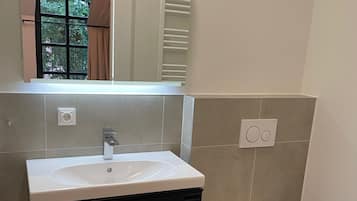 Un baño con un lavamanos blanco, un espejo, un inodoro y un cubo de basura.