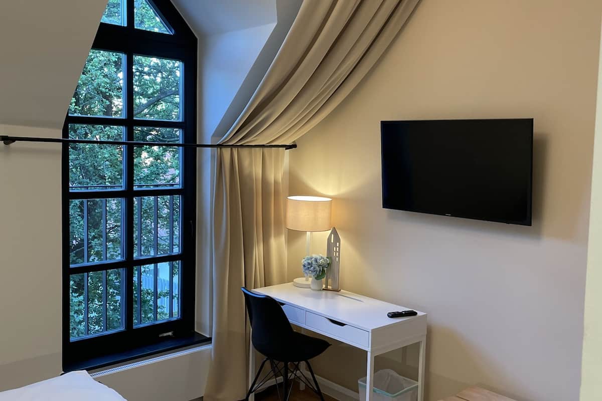A modern hotel room with a large window, a desk with a chair, a bed, and a TV mounted on the wall.