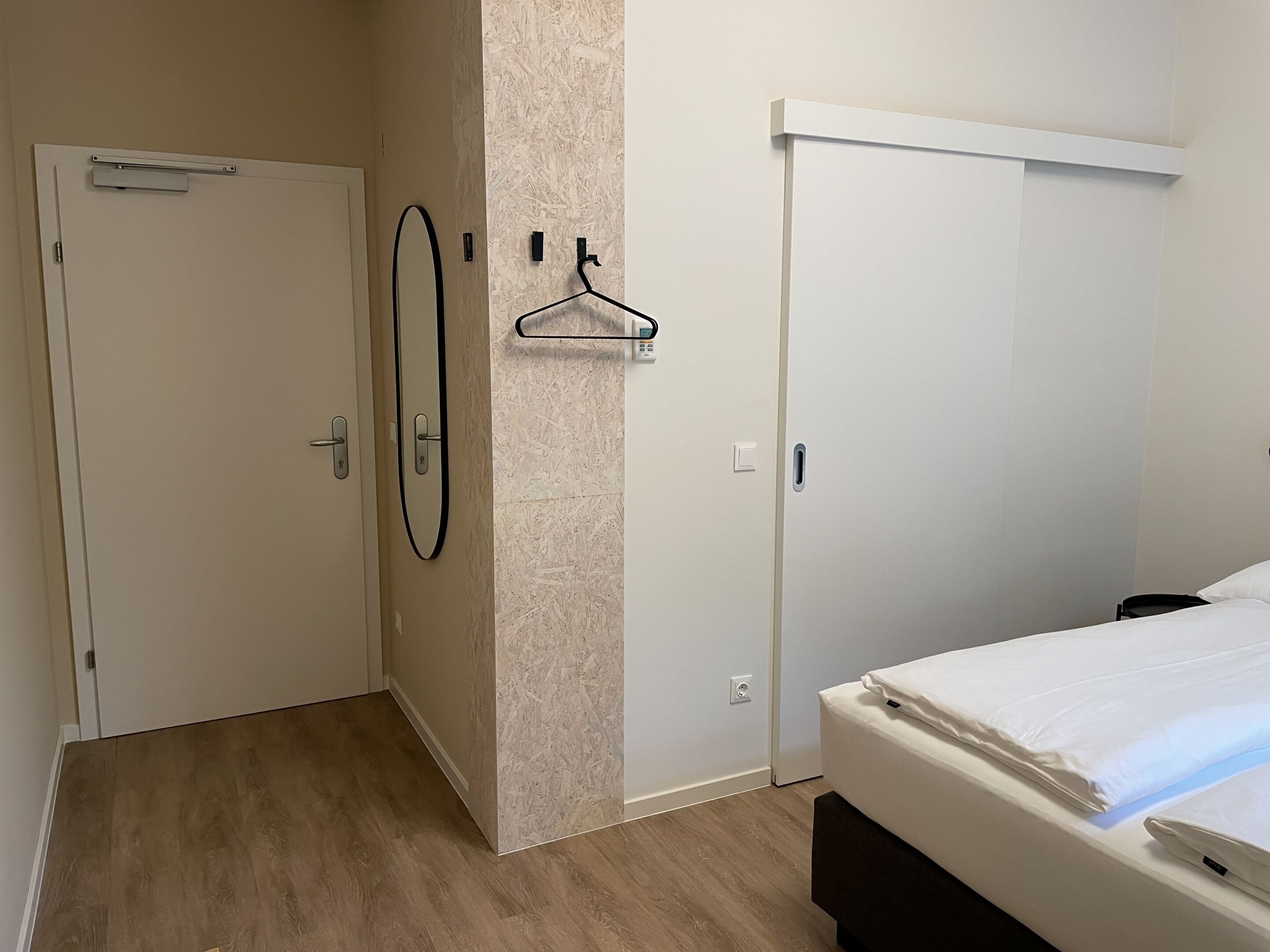 A hotel room with a bed, a wardrobe, a mirror, and a coat rack.