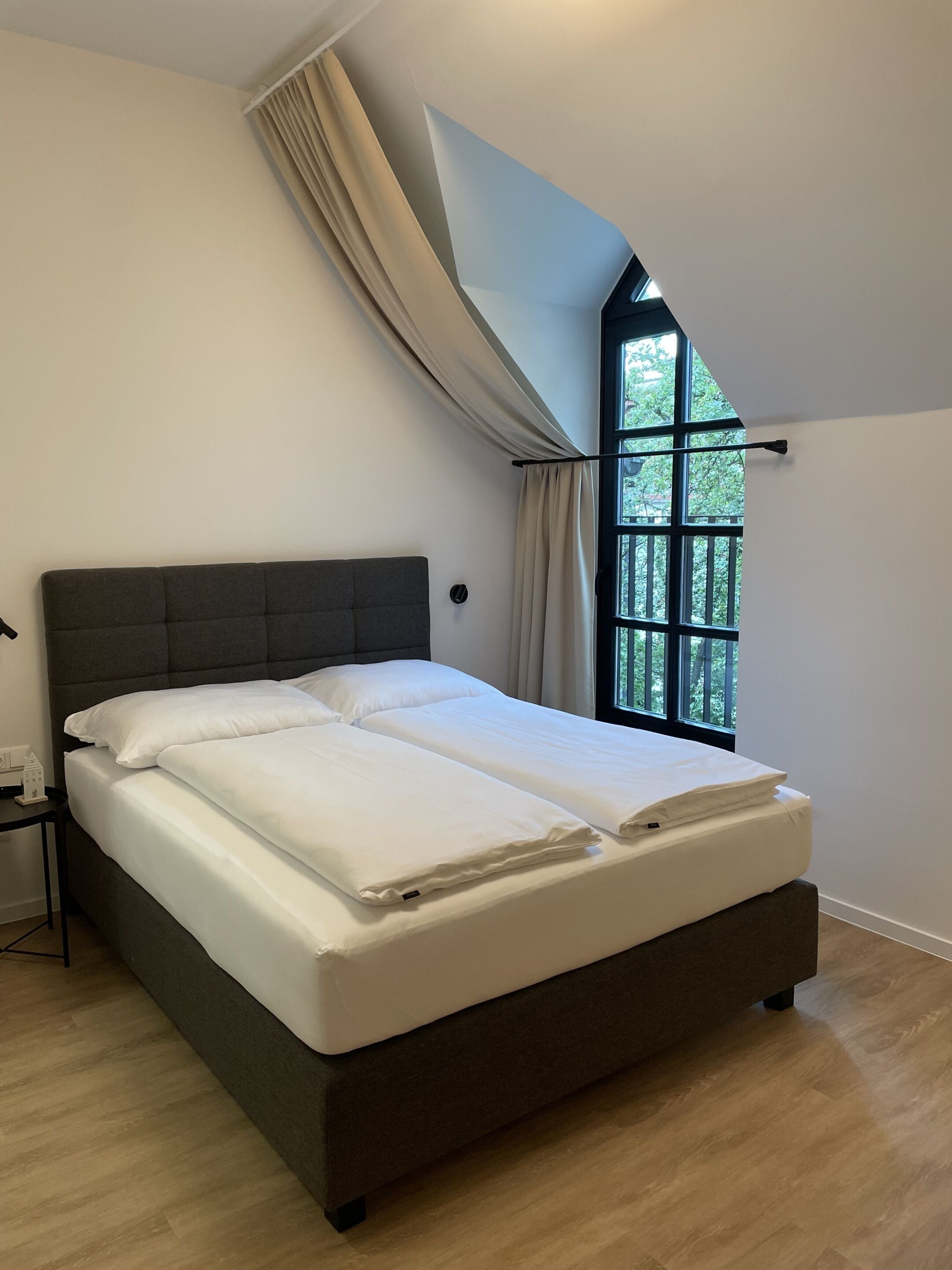 Une chambre avec un grand lit, une fenêtre avec des rideaux et une vue sur la verdure.