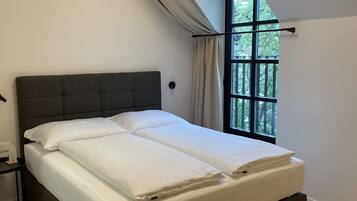 Une chambre avec un grand lit, une fenêtre avec des rideaux et une vue sur la verdure.