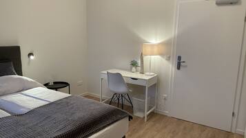 A bedroom with a bed, a desk, a chair, a lamp, and a door.