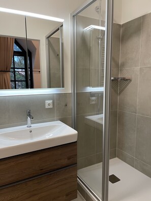 Un baño moderno con ducha de vidrio, lavamanos blanco y tocador de madera.