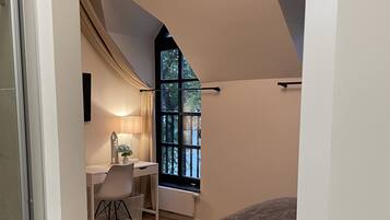 A bedroom with a bed, a desk, and a chair, a window with a view of trees, and a sloped ceiling.