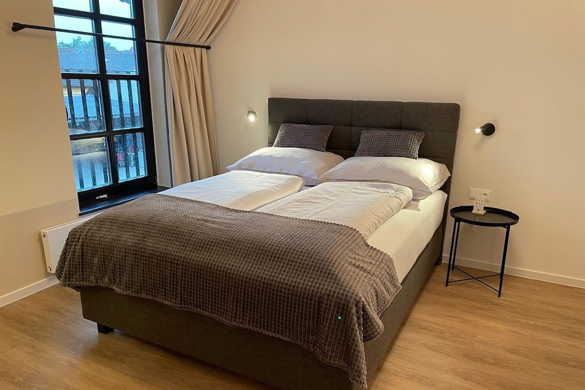 A modern bedroom with a large bed, a bedside table, and a window with curtains.