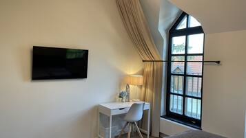 Un dormitorio con cama, escritorio, silla, televisor y ventana con cortinas.