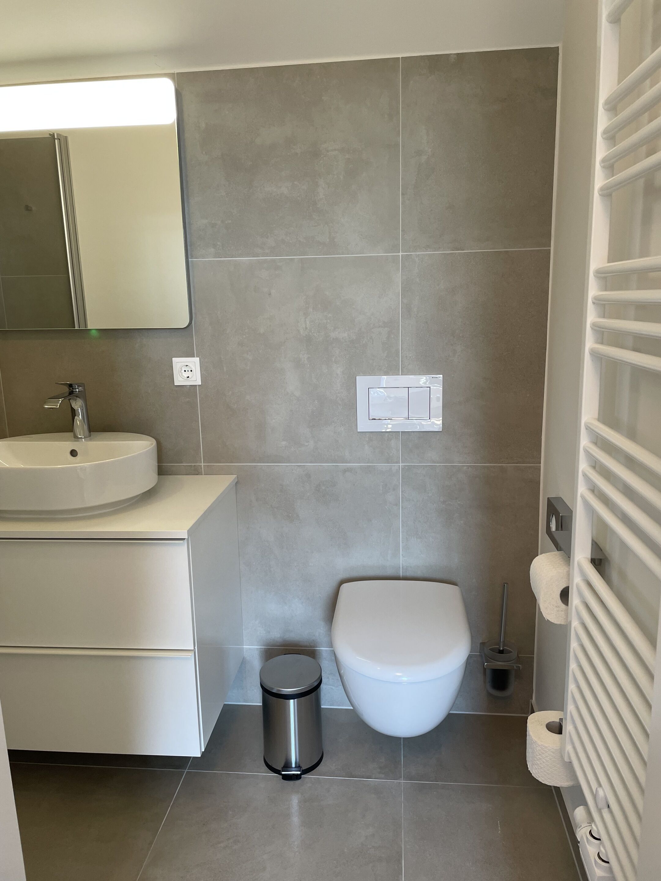 Ein modernes Badezimmer mit einem weißen Waschbecken, einer Toilette und einem Mülleimer.